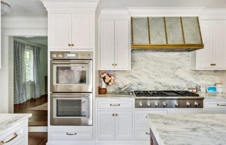 Kitchen remodel featuring custom range hood, custom white cabinetry and marble backsplash.