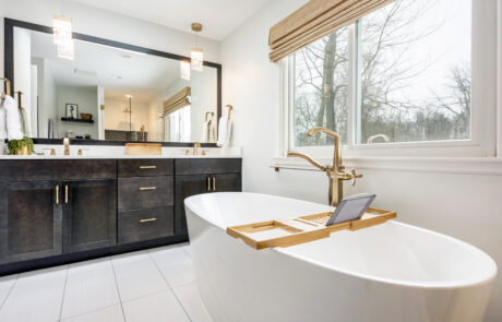 Modern bathroom with gold finishes, a freestanding tub and dark wood double vanity.